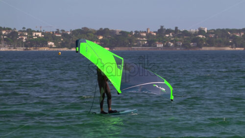Nice, France – July 5, 2025: A windsurfer gliding across the deep blue Mediterranean sea using a vibrant green and blue sail - Starpik Stock
