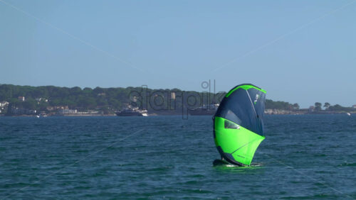 Nice, France – July 5, 2025: A windsurfer gliding across the deep blue Mediterranean sea using a vibrant green and blue sail - Starpik Stock
