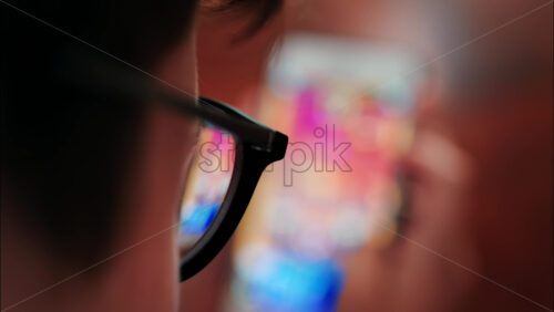 Over-the-shoulder close-up of a kid with glasses playing on a smartphone indoors - Starpik Stock