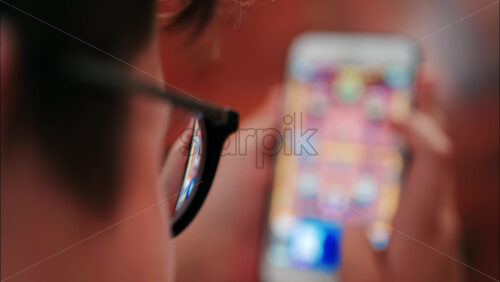 Over-the-shoulder close-up of a kid with glasses playing on a smartphone indoors - Starpik Stock