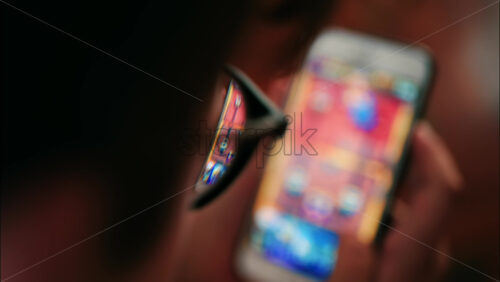 Over-the-shoulder close-up of a kid with glasses playing on a smartphone indoors - Starpik Stock