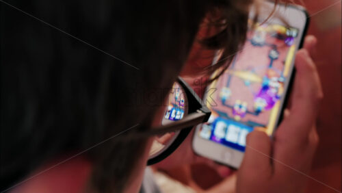 Over-the-shoulder close-up of a kid with glasses playing on a smartphone indoors - Starpik Stock
