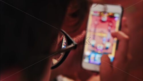 Over-the-shoulder close-up of a kid with glasses playing on a smartphone indoors - Starpik Stock