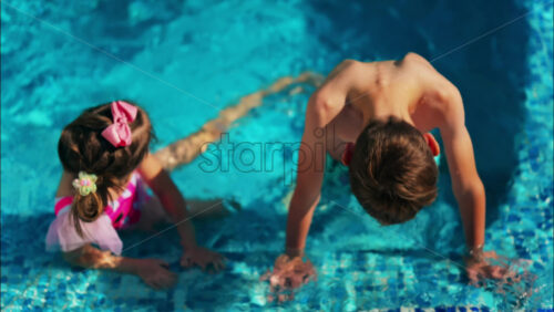 Overhead shot of a young boy and girl playing in a bright blue swimming pool - Starpik Stock