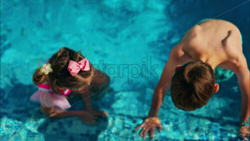 Overhead shot of a young boy and girl playing in a bright blue swimming pool - Starpik Stock