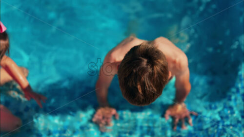 Overhead shot of a young boy and girl playing in a bright blue swimming pool - Starpik Stock
