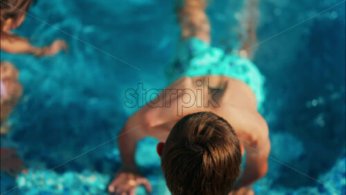 Overhead shot of a young boy and girl playing in a bright blue swimming pool - Starpik Stock