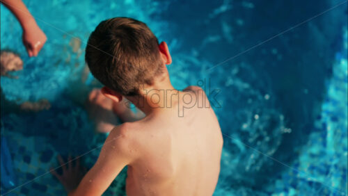Overhead shot of a young boy and girl playing in a bright blue swimming pool - Starpik Stock