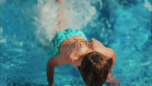 Overhead shot of a young boy playing in a bright blue swimming pool - Starpik Stock