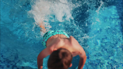Overhead shot of a young boy playing in a bright blue swimming pool - Starpik Stock