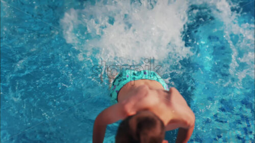 Overhead shot of a young boy playing in a bright blue swimming pool - Starpik Stock