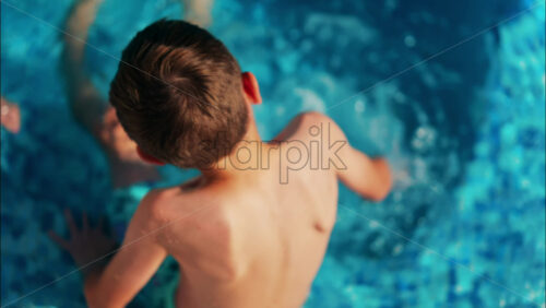 Overhead shot of a young boy playing in a bright blue swimming pool - Starpik Stock