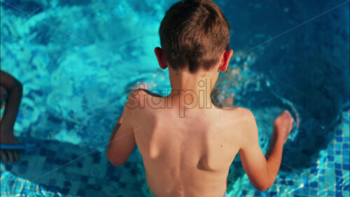 Overhead shot of a young boy playing in a bright blue swimming pool - Starpik Stock