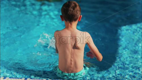 Overhead shot of a young boy playing in a bright blue swimming pool - Starpik Stock