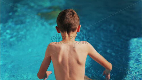 Overhead shot of a young boy playing in a bright blue swimming pool - Starpik Stock
