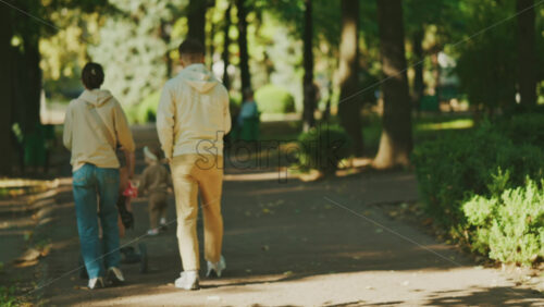 Parents walking with a stroller and toddler in a sunny park - Starpik Stock