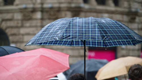 People holding umbrellas walking in the rain on thee street in Milan, Italy - Starpik Stock
