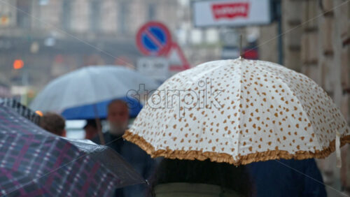 People holding umbrellas walking in the rain on thee street in Milan, Italy - Starpik Stock