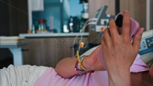 Pregnant woman scrolling on her phone while lying in a hospital bed at the doctor’s office - Starpik Stock