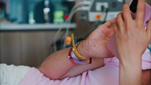 Pregnant woman scrolling on her phone while lying in a hospital bed at the doctor’s office - Starpik Stock