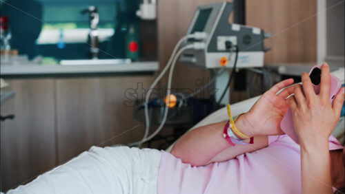 Pregnant woman scrolling on her phone while lying in a hospital bed at the doctor’s office - Starpik Stock