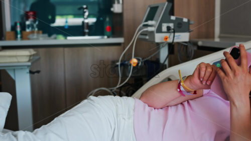 Pregnant woman scrolling on her phone while lying in a hospital bed at the doctor’s office - Starpik Stock