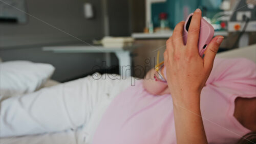 Pregnant woman scrolling on her phone while lying in a hospital bed at the doctor’s office - Starpik Stock