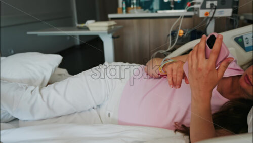 Pregnant woman scrolling on her phone while lying in a hospital bed at the doctor’s office - Starpik Stock
