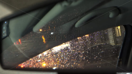 Rain dripping down the window of a moving car in the evening reflected in the rearview mirror - Starpik Stock