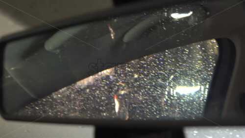 Rain dripping down the window of a moving car in the evening reflected in the rearview mirror - Starpik Stock