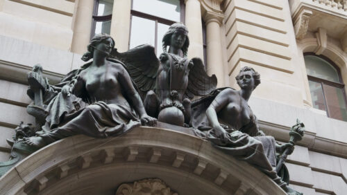 Sculptural group of bronze female and winged figures sitting atop an arched stone building entrance in London, England - Starpik Stock