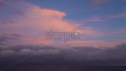 Serene view of the moon and pastel pink clouds over the Mediterranean Sea at dusk - Starpik Stock