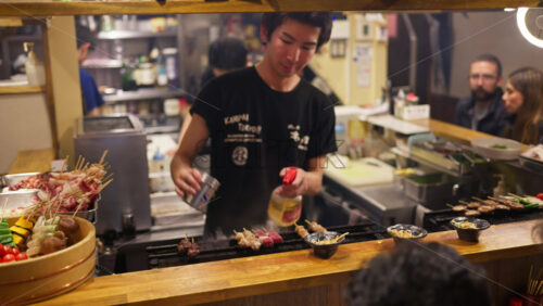 Shinjuku, Japan – April 12, 2025: Chef cooking and people sitting at a traditional Japanese restaurant on the Omoide Yokocho Memory Lane in the evening - Starpik Stock