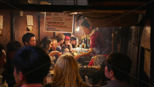 Shinjuku, Japan – April 12, 2025: Chef cooking and people sitting at a traditional Japanese restaurant on the Omoide Yokocho Memory Lane in the evening - Starpik Stock