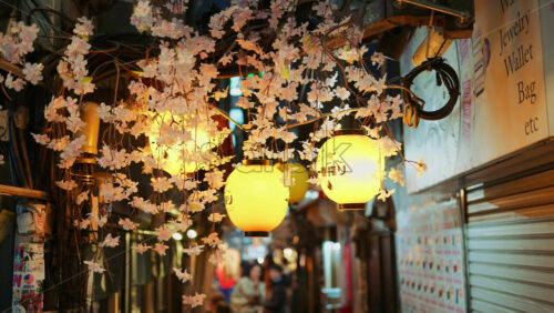 Shinjuku, Japan – April 12, 2025: Lighted paper lanterns hanging with cherry blossom flower decorations on the on the Omoide Yokocho Memory Lane in the evening. Translation: “Restaurant name” - Starpik Stock