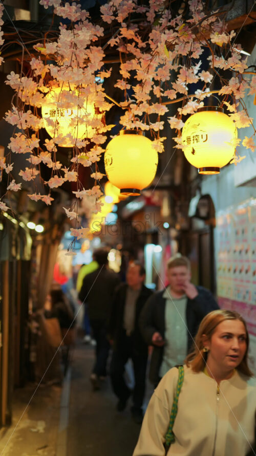 Shinjuku, Japan – April 12, 2025: Lighted paper lanterns hanging with cherry blossom flower decorations on the on the Omoide Yokocho Memory Lane in the evening. Translation:”Restaurant name”. Vertical - Starpik Stock