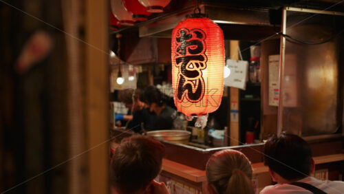 Shinjuku, Japan – April 12, 2025: People sitting at a traditional Japanese restaurant on the Omoide Yokocho Memory Lane in the evening. Translation: “Izakaya” - Starpik Stock