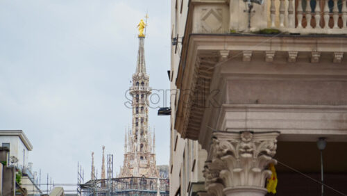 Side view of the top of the Duomo with people walking through the square in daylight - Starpik Stock
