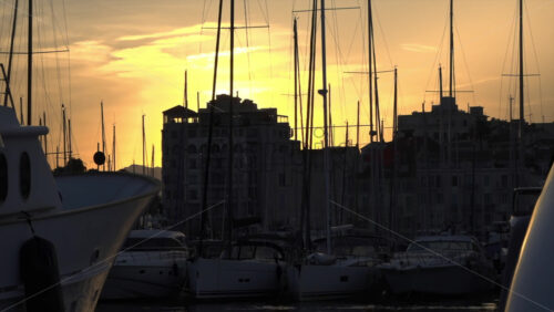 Silhouettes of sailboat masts and yachts against a golden sunset sky in the Cannes marina - Starpik Stock