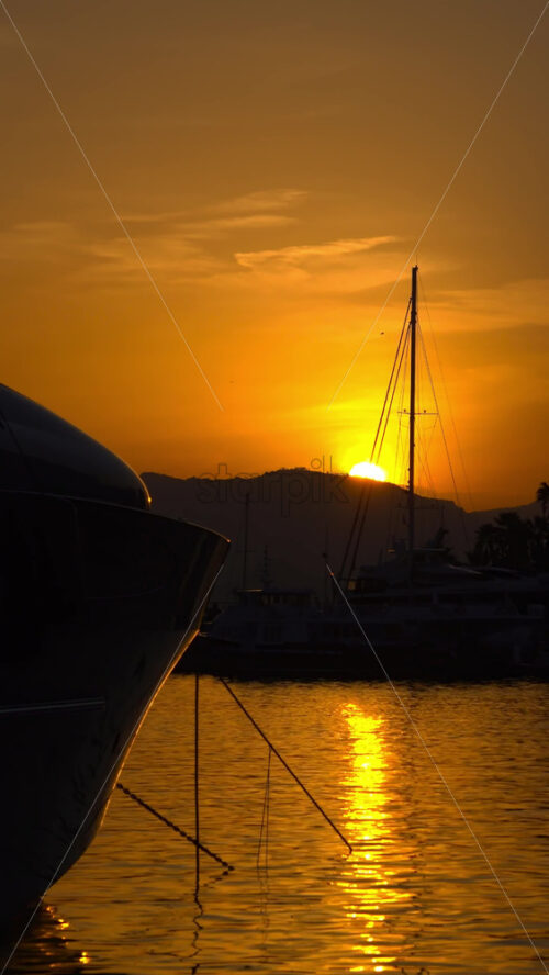 Silhouettes of sailboat masts and yachts against a golden sunset sky in the Cannes marina. Vertical - Starpik Stock