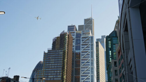 Skyline of London featuring the Gherkin, Leadenhall Building, and other modern skyscrapers under clear sky. Airplane passing by - Starpik Stock