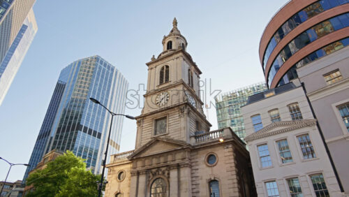 St. Botolph-without-Bishopsgate church standing prominently at the edge of Liverpool Street, framed by gleaming glass towers in London, England - Starpik Stock
