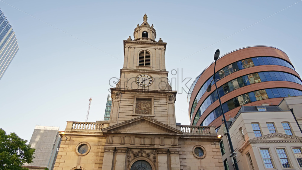 St. Botolph-without-Bishopsgate church standing prominently at the edge of Liverpool Street, framed by gleaming glass towers in London, England - Starpik Stock