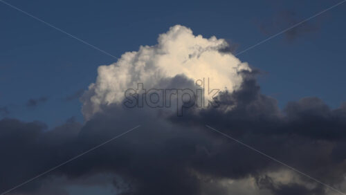 Sunlit white cloud rising above a layer of darker clouds against a deep blue sky - Starpik Stock