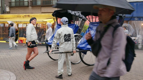 Taito, Japan – April 13. 2025: Rickshaw runners talking to the people on rickshaws on the street, near the Asakusa, Kannon Dori Market - Starpik Stock