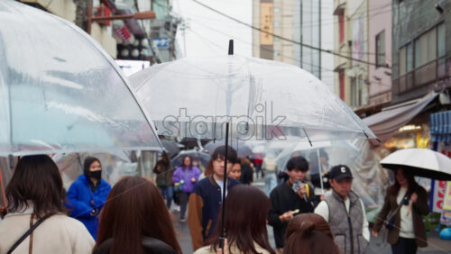 Taito, Japan – April 13. 2025: Slow motion of people holding umbrellas walking through the Asakusa, Kannon Dori Market on a rainy day - Starpik Stock