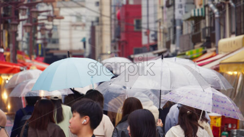 Taito, Japan – April 13. 2025: Slow motion of people holding umbrellas walking through the Asakusa, Kannon Dori Market on a rainy day - Starpik Stock