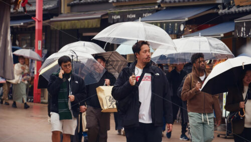 Taito, Japan – April 13. 2025: Slow motion of people holding umbrellas walking through the Asakusa, Kannon Dori Market on a rainy day - Starpik Stock