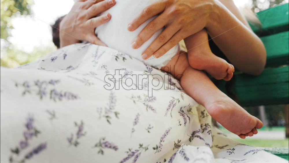 Tender moment of a mother breastfeeding her baby on a green park bench in daylight - Starpik Stock