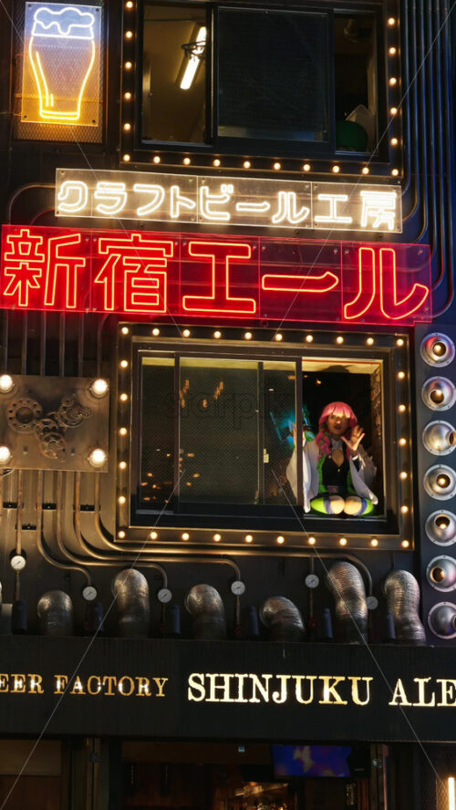 Tokyo, Japan – April 12, 2025: Girl with pink hair waving from the window of the Craft Beer Factory Shinjuku Ale in the evening. Translation: “Craft Beer Factory Shinjuku Ale”. Vertical - Starpik Stock